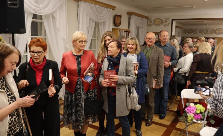 kolorowe zdjęcie, grupa ludzi siedzi na krzesłach, zdjęcie na tle książek
