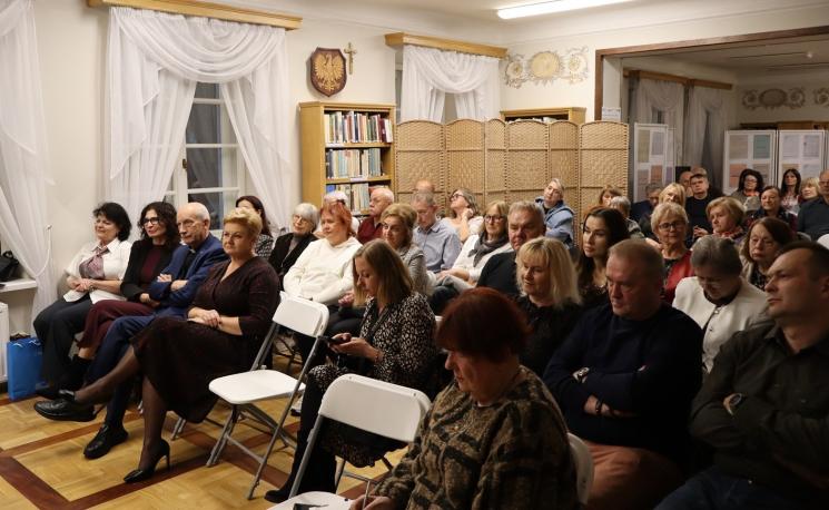 kolorowe zdjęcie, grupa ludzi siedzi na krzesłach, zdjęcie na tle książek
