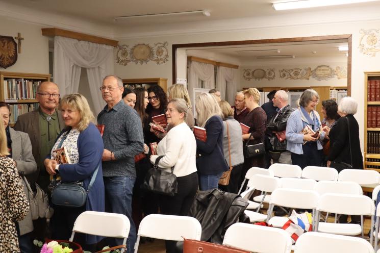 kolorowe zdjęcie, grupa ludzi siedzi na krzesłach, zdjęcie na tle książek