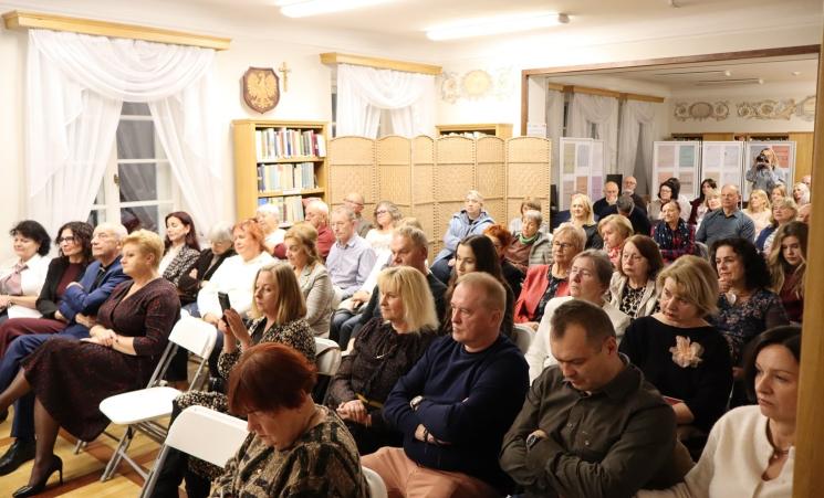 kolorowe zdjęcie, grupa ludzi siedzi na krzesłach, zdjęcie na tle książek