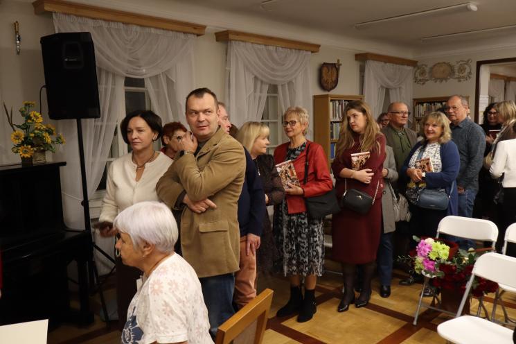 kolorowe zdjęcie, grupa ludzi siedzi na krzesłach, zdjęcie na tle książek