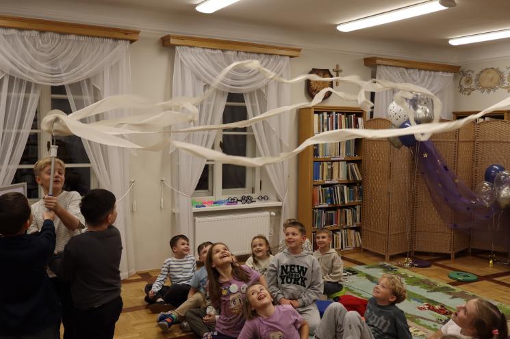 kolorowe zdjęcie, 2 osoby dorosłe, napis Noc Bibliotek, Pan Profesorek, dzieci siedzą na dywanie i poduszkach,