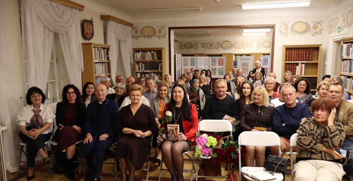 kolorowe zdjęcie, grupa ludzi siedzi na krzesłach, zdjęcie na tle książek