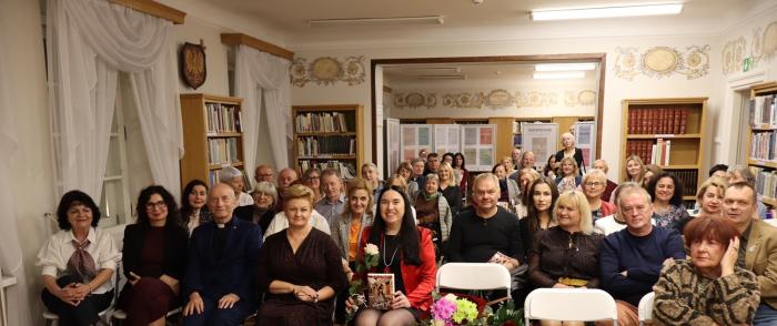 kolorowe zdjęcie, grupa ludzi siedzi na krzesłach, zdjęcie na tle książek