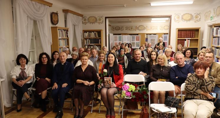 kolorowe zdjęcie, grupa ludzi siedzi na krzesłach, zdjęcie na tle książek