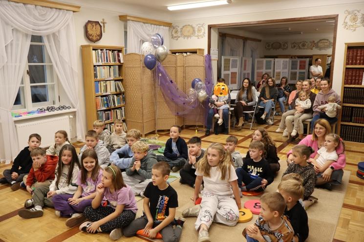 kolorowe zdjęcie, 2 osoby dorosłe, napis Noc Bibliotek, Pan Profesorek, dzieci siedzą na dywanie i poduszkach,