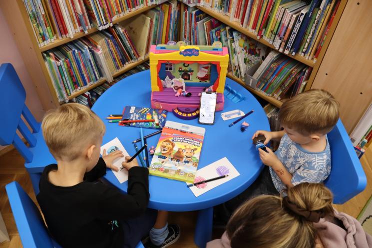 kolorowe zdjęcie, 2 osoby dorosłe, napis Noc Bibliotek, Pan Profesorek, dzieci siedzą na dywanie i poduszkach,