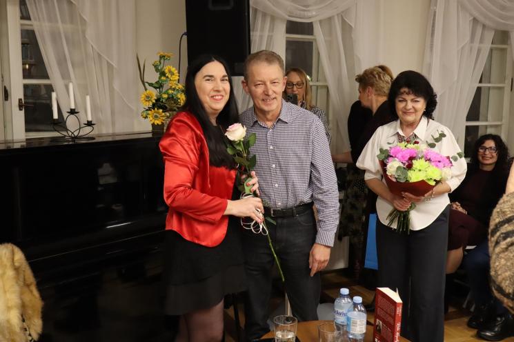 kolorowe zdjęcie, grupa ludzi siedzi na krzesłach, zdjęcie na tle książek