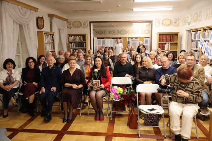 kolorowe zdjęcie, grupa ludzi siedzi na krzesłach, zdjęcie na tle książek